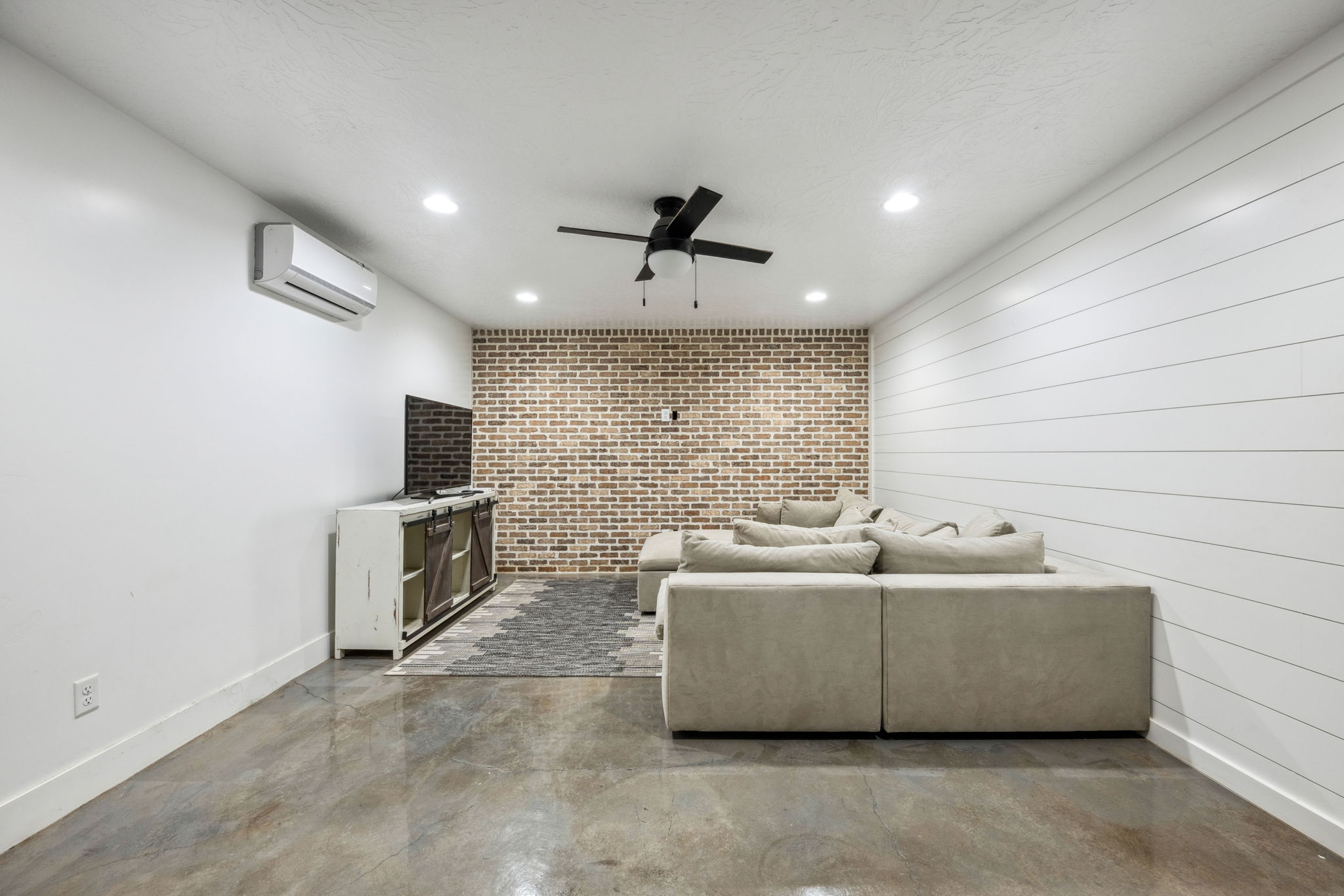 Living room featuring finished concrete floors, brick wall, recessed lighting, a ceiling fan, and an accent wall