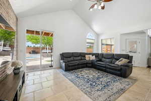 Living area with ceiling fan, high vaulted ceiling, and stone tile flooring