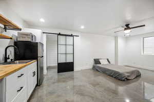 Bedroom featuring a barn door, finished concrete flooring, freestanding refrigerator, a ceiling fan, and recessed lighting