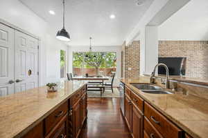 Kitchen with a textured ceiling, light stone counters, pendant lighting, dark wood finished floors, and brown cabinetry