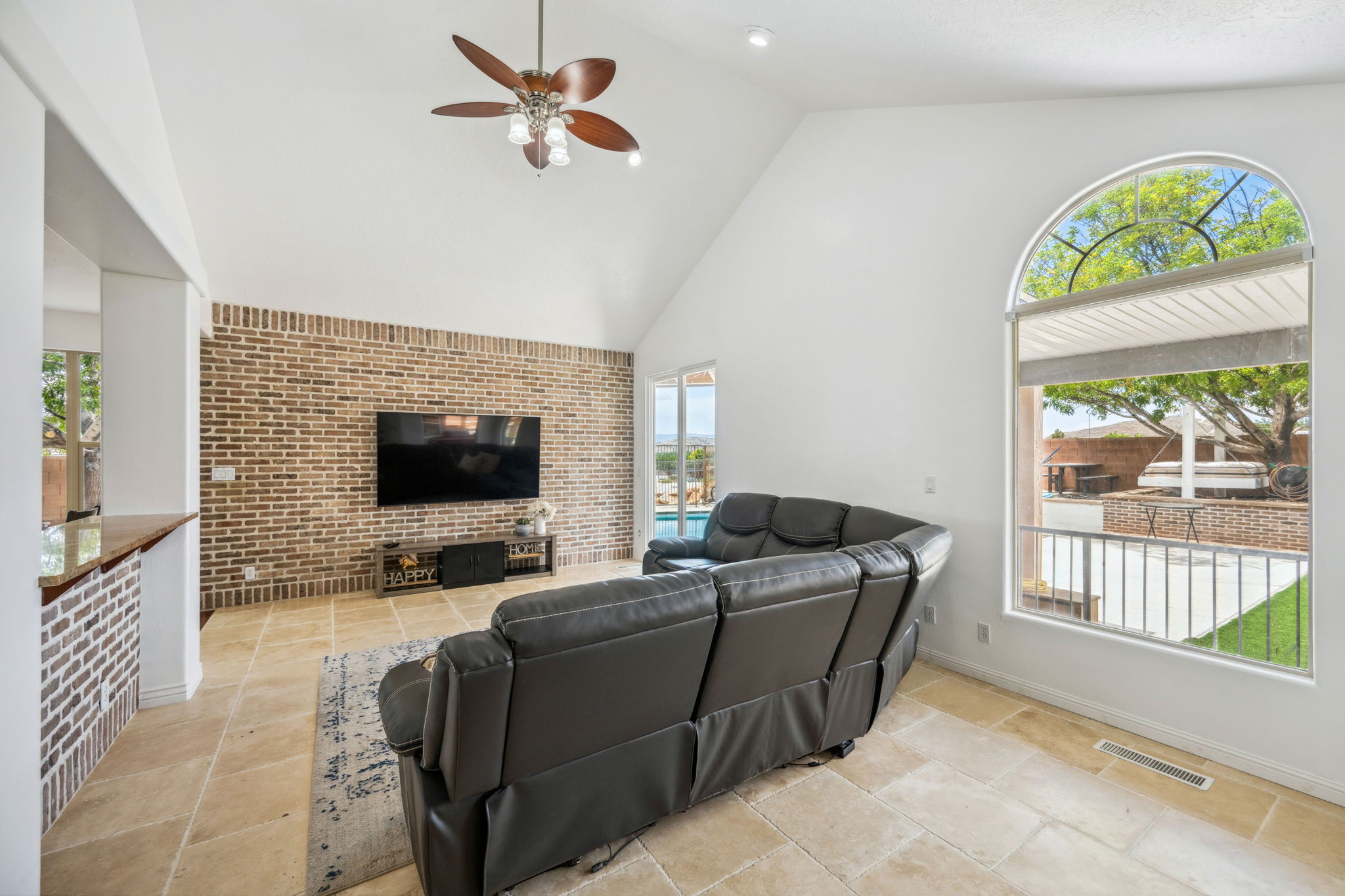 Living room with high vaulted ceiling, ceiling fan, and brick wall