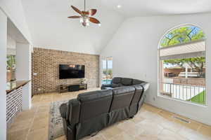 Living room with high vaulted ceiling, ceiling fan, and brick wall