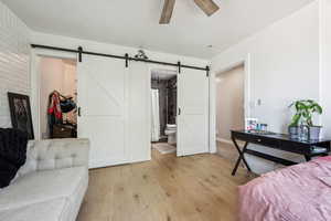 Bedroom featuring light wood-style floors, a spacious closet, ensuite bath, ceiling fan, and a barn door