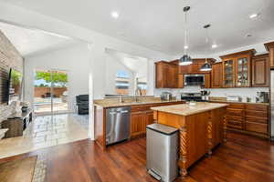 Kitchen featuring brown cabinets, light stone countertops, stainless steel appliances, a kitchen island, and hanging light fixtures