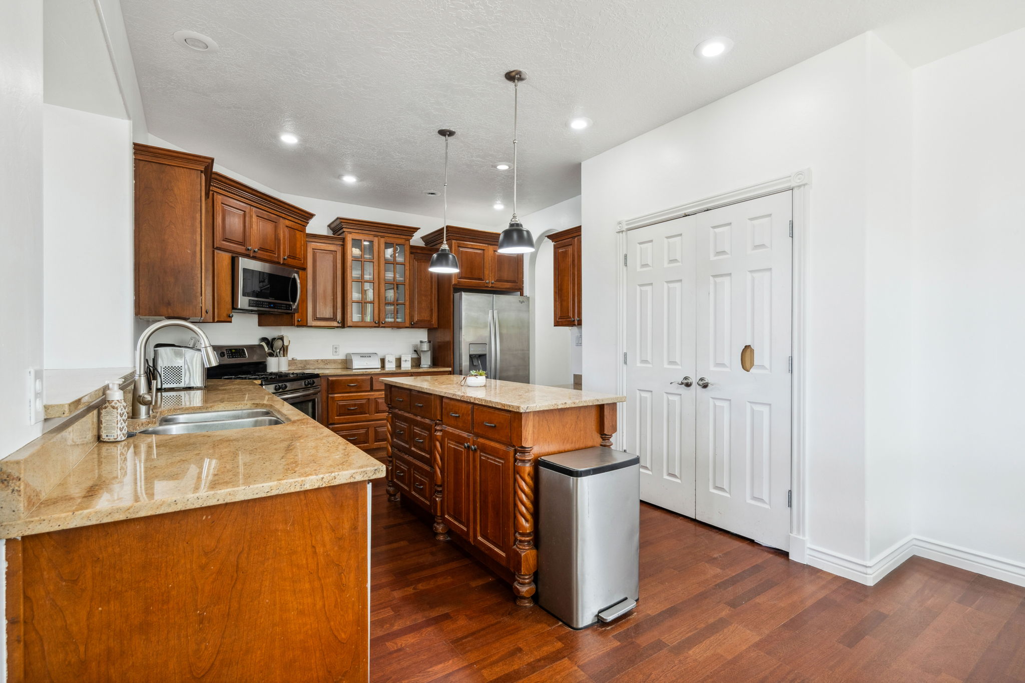 Kitchen with light stone countertops, brown cabinets, decorative light fixtures, recessed lighting, and glass insert cabinets