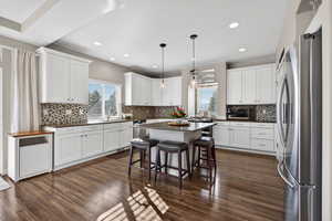 Kitchen featuring appliances with stainless steel finishes, hanging light fixtures, a kitchen breakfast bar, white cabinets, and recessed lighting