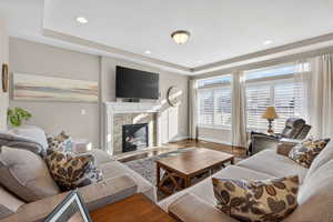 Living room with a premium fireplace, wood finished floors, a tray ceiling, recessed lighting, and a textured ceiling