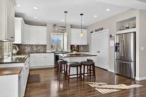 Kitchen with stainless steel appliances, a breakfast bar area, decorative light fixtures, white cabinets, and recessed lighting