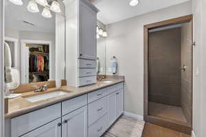 Primary Full bathroom featuring a textured ceiling, a walk in closet, double vanity, and a stall shower