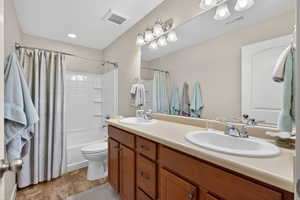 Bathroom featuring double vanity, shower / bathtub combination with curtain, and a textured ceiling