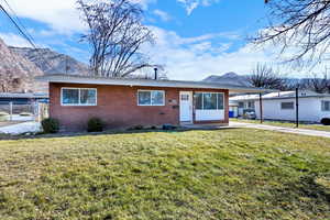 Ranch-style house featuring brick siding, a front lawn, a mountain view, an attached carport, and concrete driveway