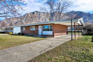 Ranch-style house featuring an attached carport, a front yard, a mountain view, and brick siding