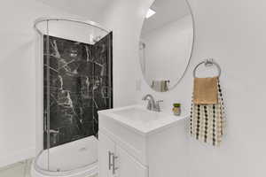 Full bath featuring marble look tiles, vanity, and a marble finish shower