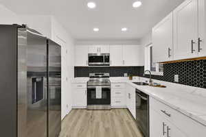 Kitchen with stainless steel appliances, light stone counters, white cabinets, recessed lighting, and light wood-type flooring