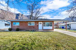 Ranch-style house with brick siding, a mountain view, a front lawn, an attached carport, and concrete driveway