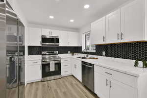 Kitchen featuring appliances with stainless steel finishes, light stone countertops, white cabinetry, light wood-type flooring, and recessed lighting