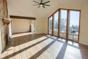 Unfurnished living room featuring wood finished floors, vaulted ceiling, a stone fireplace, and ceiling fan