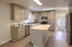 Kitchen featuring stainless steel appliances, wooden counters, light wood-style floors, and a center island