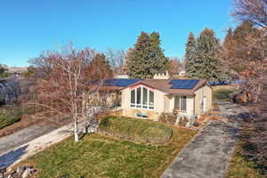 View of front of home with roof mounted solar panels and a front lawn