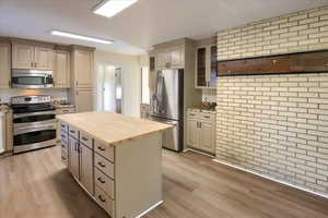 Kitchen with stainless steel appliances, brick wall, butcher block counters, glass insert cabinets, and cream cabinets