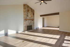 Unfurnished living room featuring lofted ceiling, a stone fireplace, wood finished floors, and a ceiling fan
