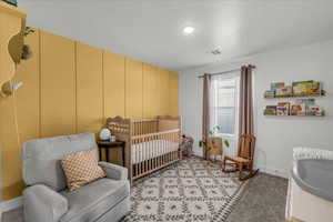 Bedroom with a nursery area, light carpet, and a decorative wall