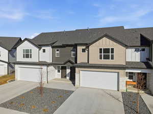 View of front of house with board and batten siding, stone siding, a residential view, concrete driveway, and roof with shingles