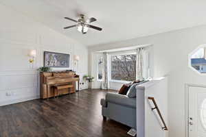 Living room with vaulted ceiling, an upstairs landing, laminate flooring, ceiling fan, and a decorative wall