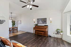 Living room featuring vaulted ceiling, laminate floors, a ceiling fan, and a chandelier