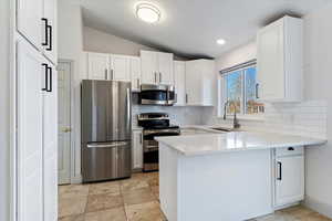 Kitchen with stainless steel appliances, light quartz counters, vaulted ceiling, a peninsula, and white cabinetry