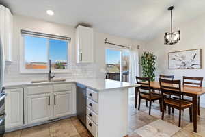 Kitchen with white cabinetry, a peninsula, light quartz countertops, backsplash, and pendant lighting
