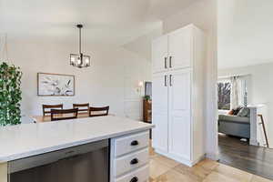 Kitchen with dishwasher, light quartz counters, vaulted ceiling, white cabinets, and pendant lighting