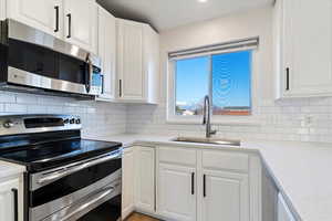 Kitchen featuring stainless steel appliances, white cabinets, light quartz counters, and decorative backsplash