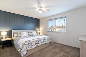 Bedroom with an accent wall, dark carpet, a ceiling fan, and wood walls