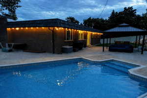 Pool at dusk featuring an outdoor living space, an outdoor pool, a gazebo, and a patio area