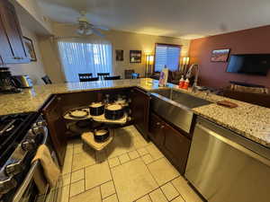 Kitchen with appliances with stainless steel finishes, light stone countertops, open floor plan, dark brown cabinetry, and a peninsula