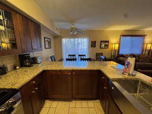 Kitchen with dark brown cabinets, glass insert cabinets, gas stove, light stone counters, and a peninsula