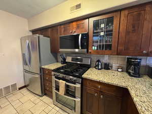 Kitchen with appliances with stainless steel finishes, light stone countertops, decorative backsplash, light tile patterned floors, and dark brown cabinets