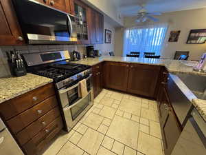 Kitchen with appliances with stainless steel finishes, light stone counters, backsplash, ceiling fan, and dark brown cabinets