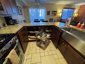 Kitchen featuring dark brown cabinets, a peninsula, double oven range, light stone counters, and light tile patterned flooring