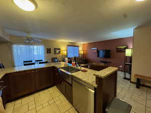 Kitchen with dark brown cabinets, dishwasher, light stone counters, open floor plan, and a kitchen dining