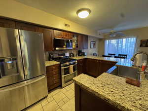 Kitchen with stainless steel appliances, light stone countertops, dark brown cabinets, and decorative backsplash