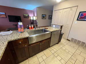 Kitchen with light stone countertops, stainless steel dishwasher, dark brown cabinets, and open floor plan