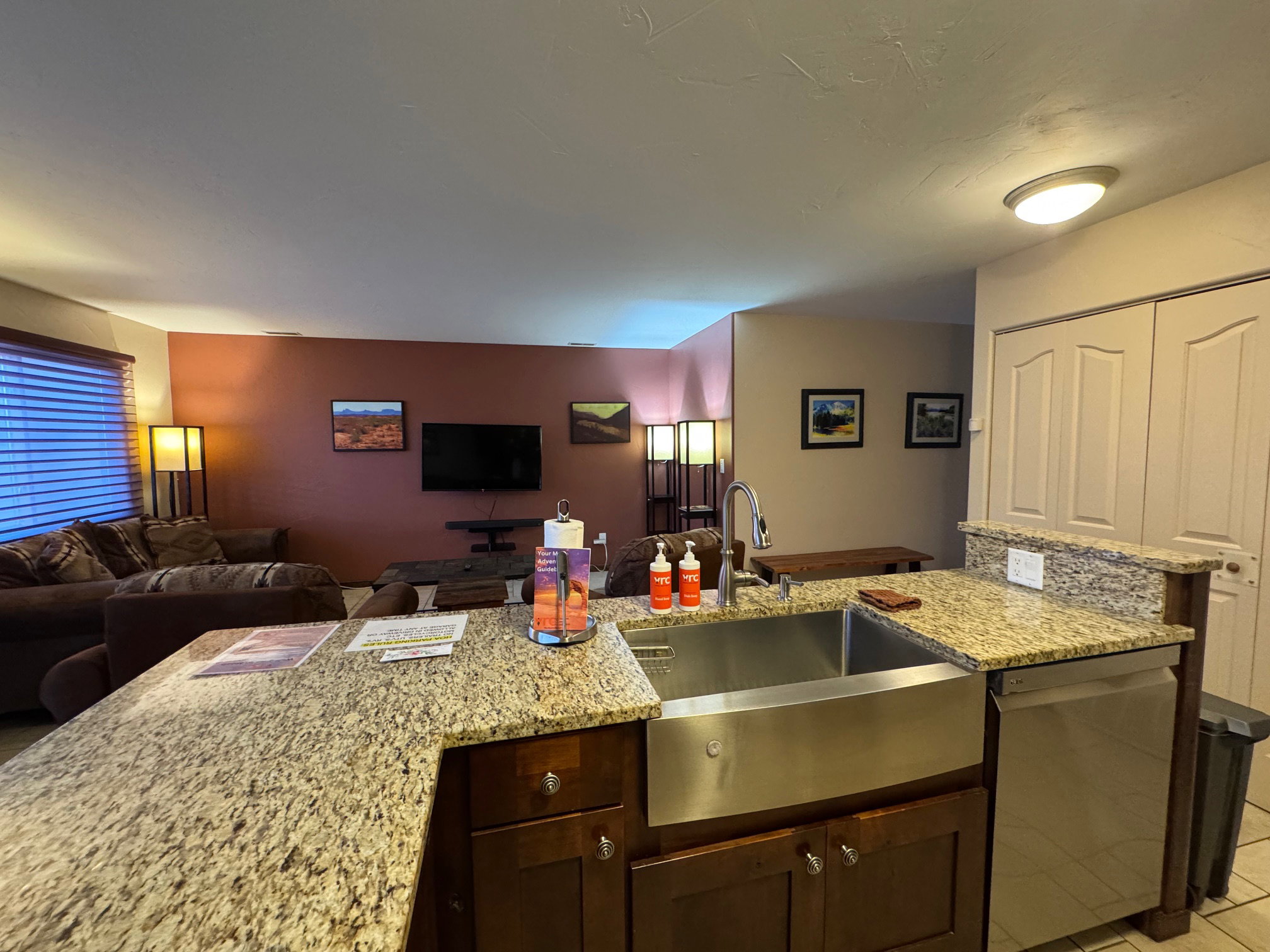 Kitchen with light stone counters, dishwasher, open floor plan, and dark brown cabinetry