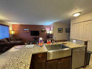 Kitchen with light stone counters, dishwasher, open floor plan, and dark brown cabinetry