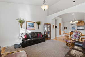 Living room featuring vaulted ceiling, arched walkways, a chandelier, ornamental molding, and light carpet