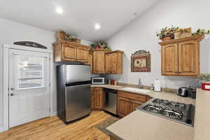 Kitchen featuring stainless steel appliances, light countertops, vaulted ceiling, light wood-style flooring, and brown cabinetry