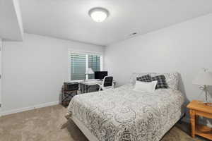 Bedroom featuring light colored carpet, an office area, and a textured ceiling