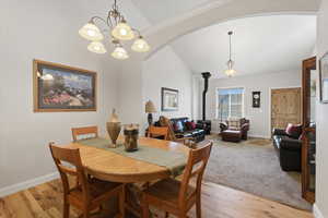 Dining area featuring a wood stove, vaulted ceiling, light wood-style floors, arched walkways, and a chandelier