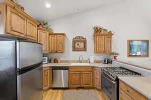 Kitchen with appliances with stainless steel finishes, light wood-type flooring, recessed lighting, light stone countertops, and brown cabinetry